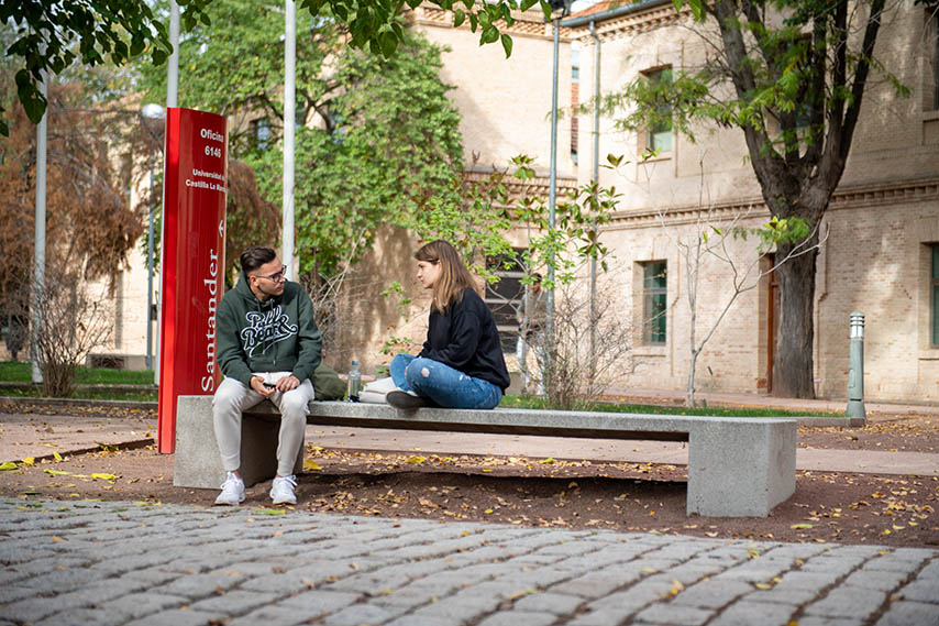 Dos estudiantes sentados en un banco del Campus de Toledo