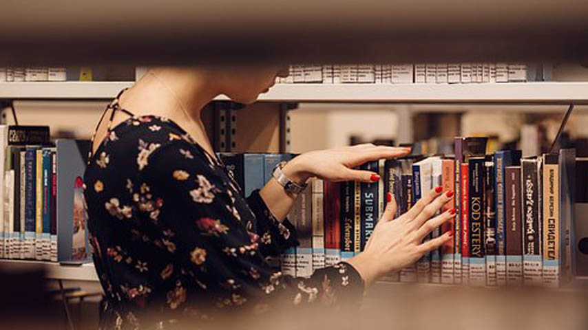 Mujer buscando libro en estante de biblioteca.