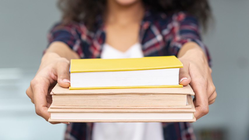 Manos de persona sujetando libros.